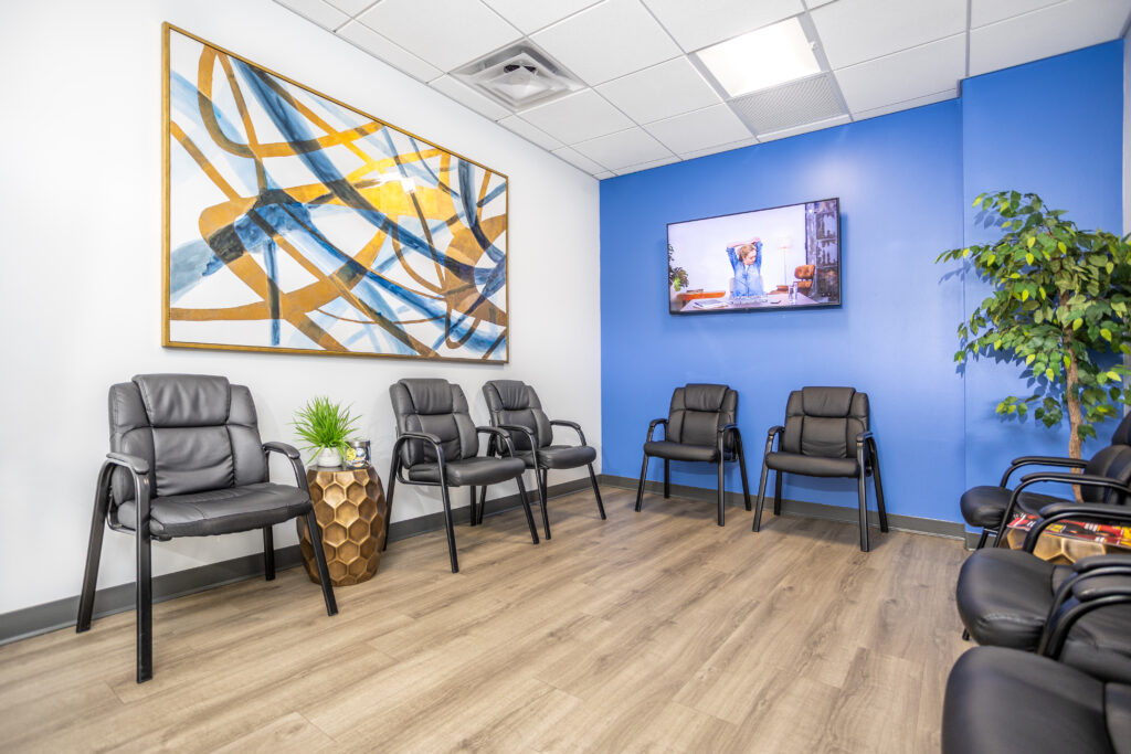 Lobby filled with black chairs, a blue accent wall with a TV and an abstract painting.