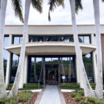 Exterior of the administrative office with tall royal palm trees lining the entrance walkway.