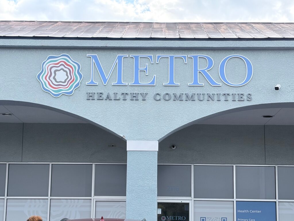 The exterior of a light blue building with a large sign that reads "METRO HEALTHY COMMUNITIES" next to the organization's swirling circle logo.