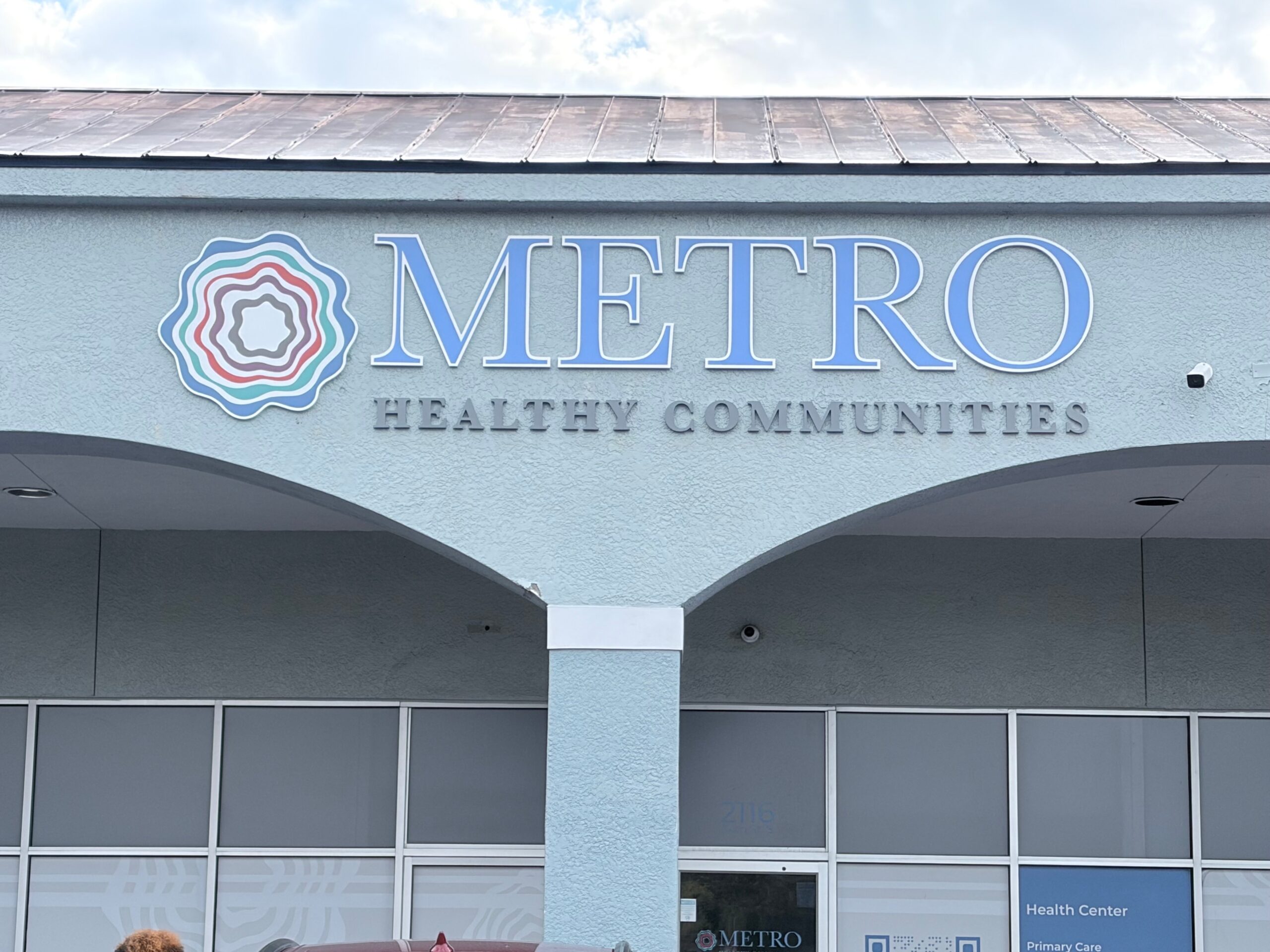 The exterior of a light blue building with a large sign that reads "METRO HEALTHY COMMUNITIES" next to the organization's swirling circle logo.