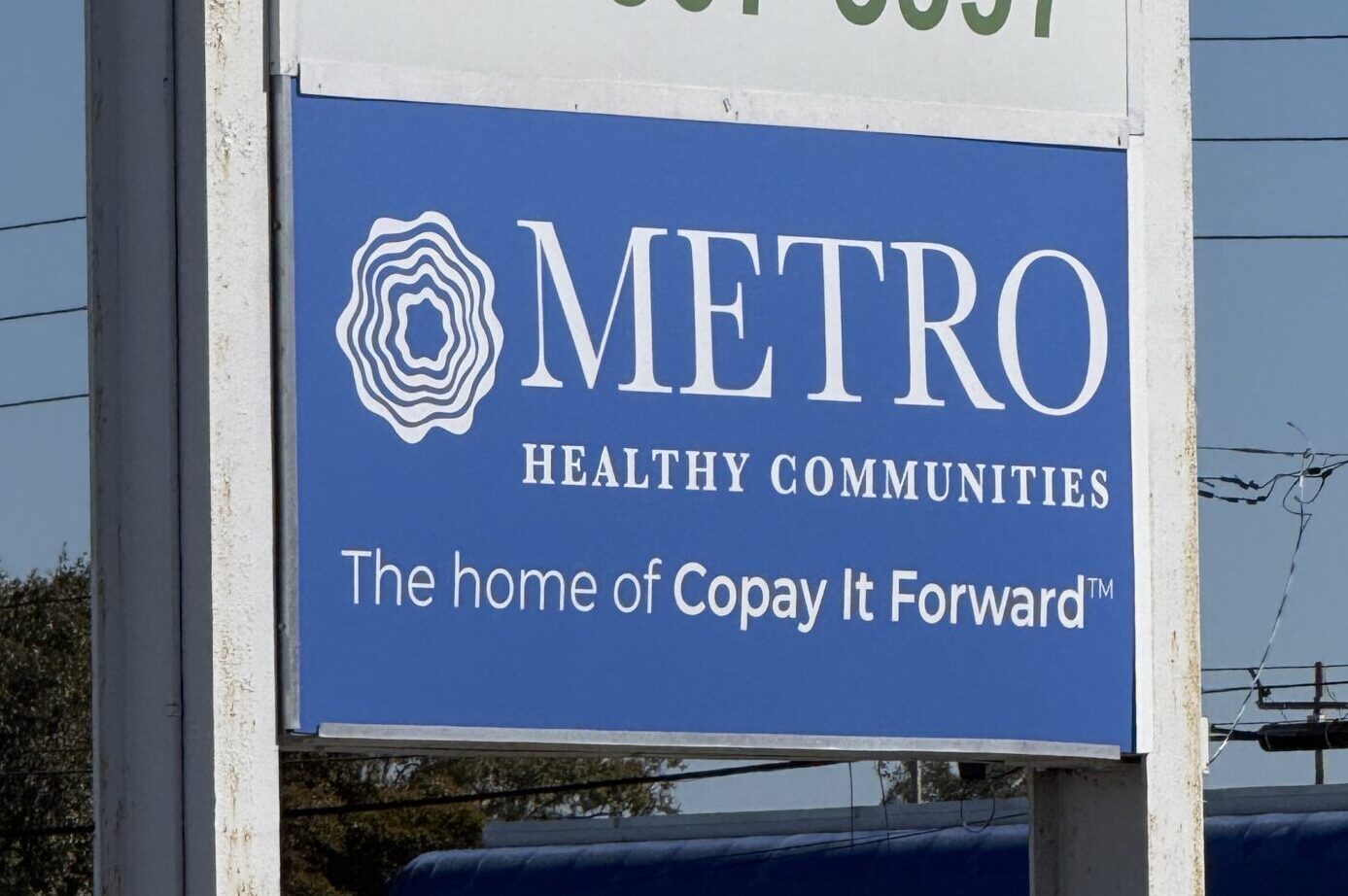 A blue outdoor sign for METRO Healthy Communities with text that reads "The home of Copay It Forward".