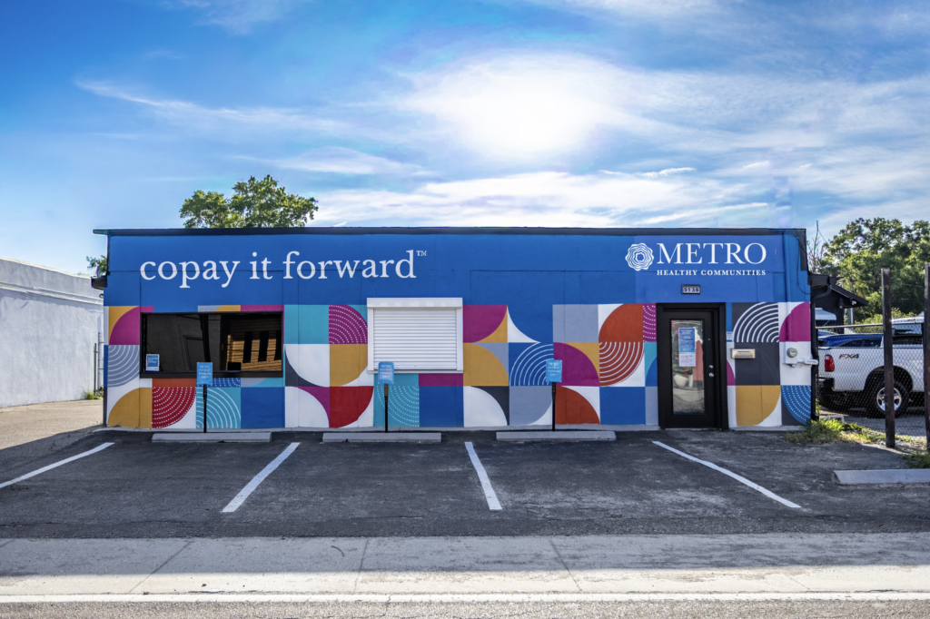 Blue building on a sunny day with a mural painted on it and the tagline "Copay It Forward" as well as the METRO logo.