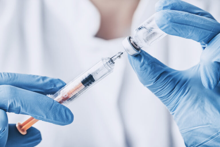 Gloved hands drawing a vaccine from a vial into a syringe.