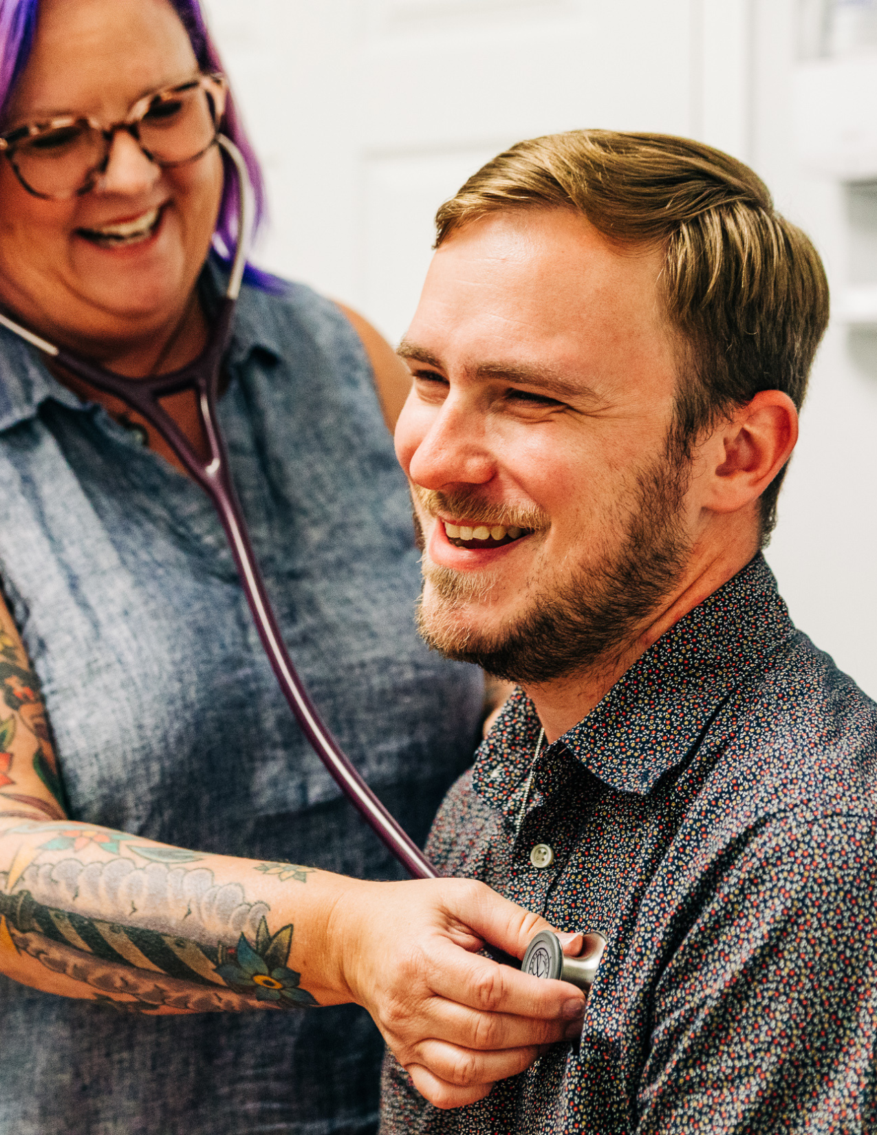 A smiling Metro healthcare provider using a stethoscope on a relaxed, happy patient.