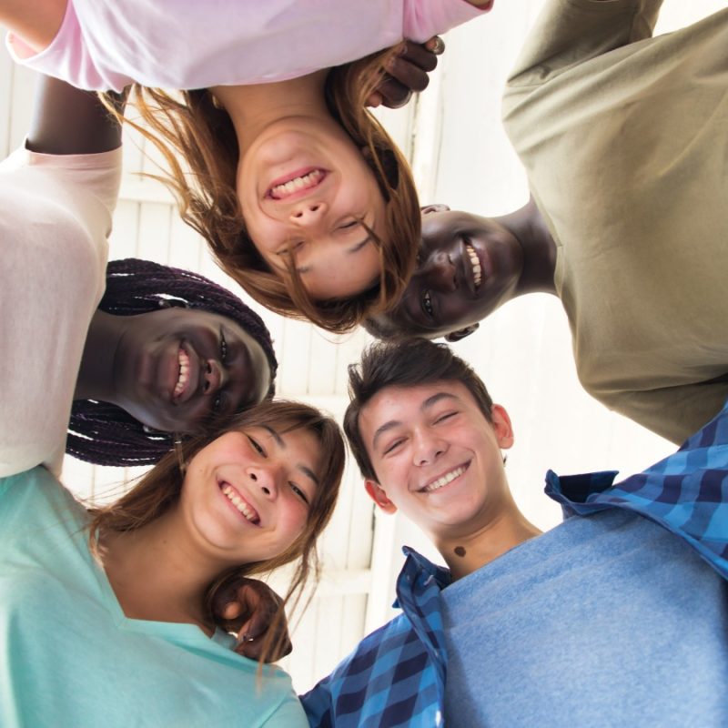 A view from below of a group of smiling young people forming a circle and looking down at the camera.