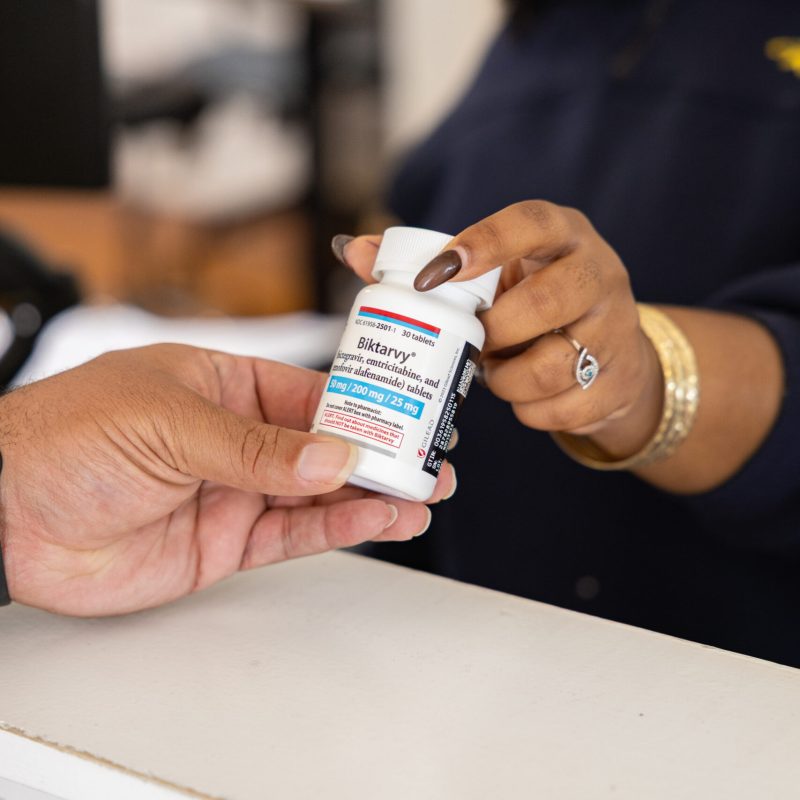 A female handing a bottle of prescription Biktarvy to a client.