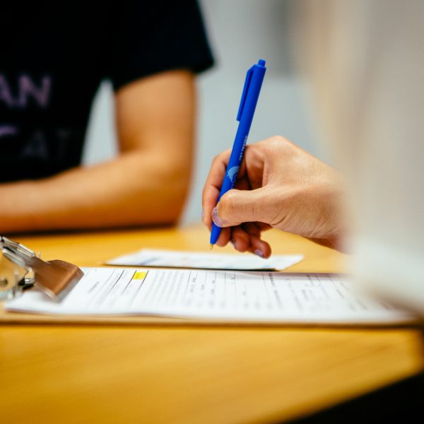 Close-up of a person's hand holding a blue pen to fill out a form on a clipboard.
